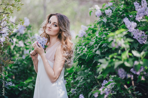 Beautiful young woman with long curly hair posing with lilacs