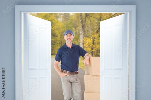 Happy delivery man leaning on pile of cardboard boxes