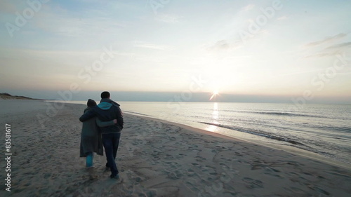 Slow motion of young couple in love walking slowly step by step side by side along coastline on the beach with wet sand by the sea, watching sunset and talking