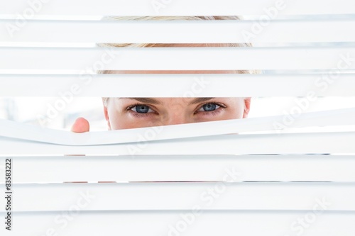 Curious blonde woman looking through venetian blind