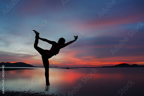 Silhouette of young woman practicing yoga on the lake at sunset