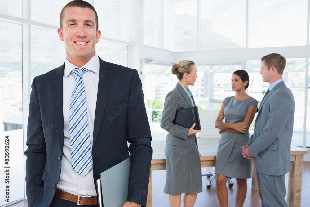 Businessman smiling at camera with colleagues behind him Businessman smiling at camera with colleagues behind him