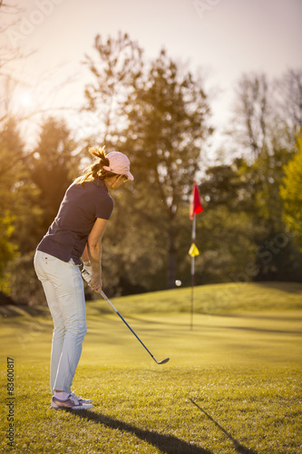 Female golf player pitching towards flag.