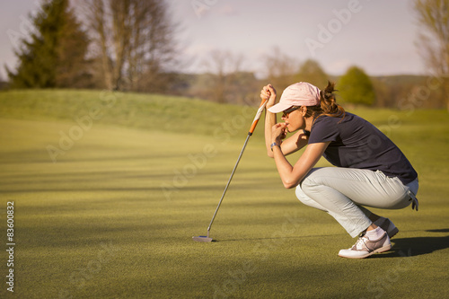Female golf player squatting on green.