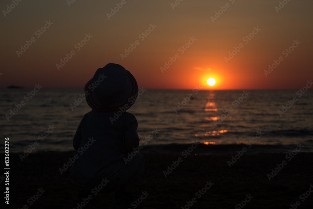 child sitting on his haunches and enjoy the sunset on the sea
