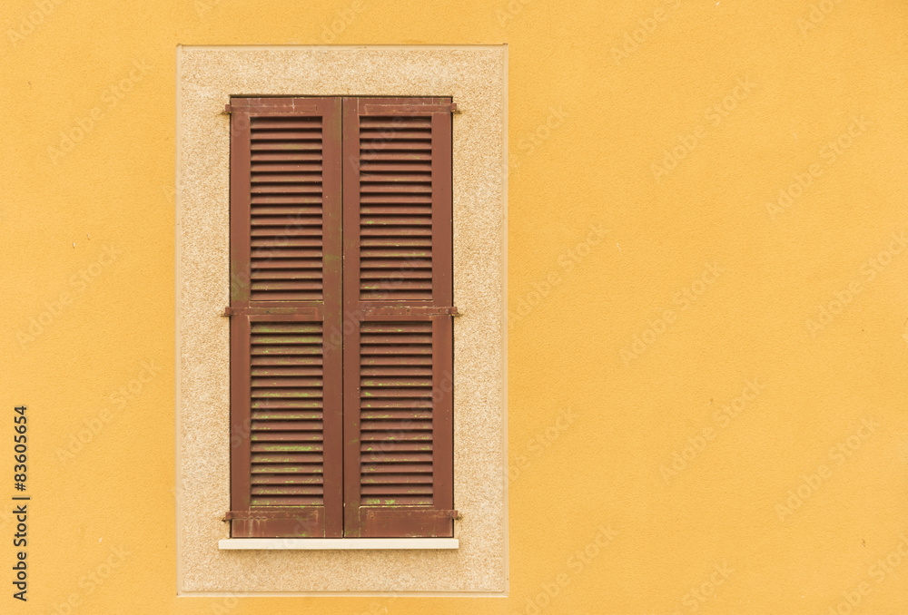 Braune Fensterläden geschlossen mit gelber Fassade
