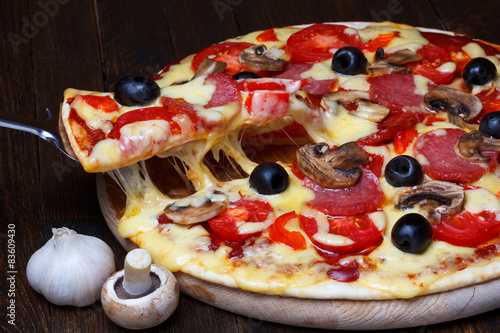 Lifted pizzza slice with melting cheese on dark wooden table photo