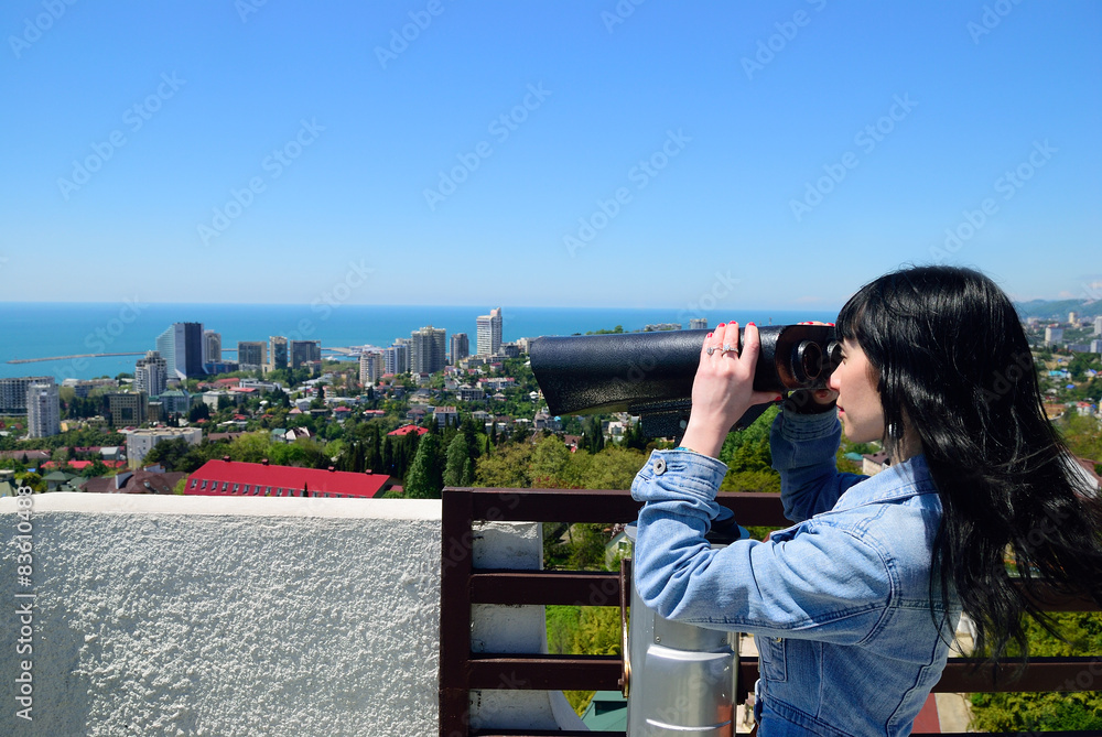 Girl on the observation deck looking into binokol. Far coast of