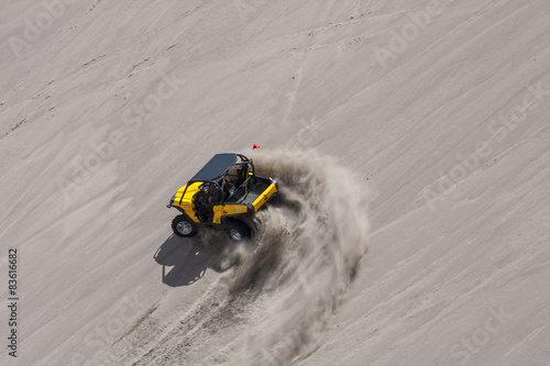Fotografie Yellow side by side buggy racing by in the sand dunes