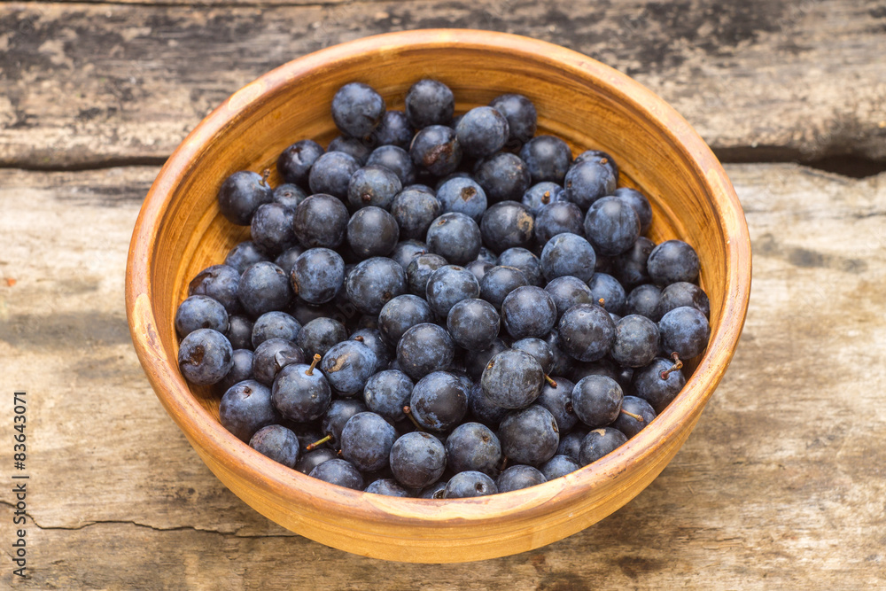 Ripe blackthorn berries in clay bowl on wood background Ripe blackthorn berries in clay bowl on wood background
