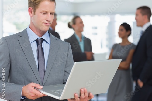 Businessman working on laptop with colleagues behind him © WavebreakmediaMicro