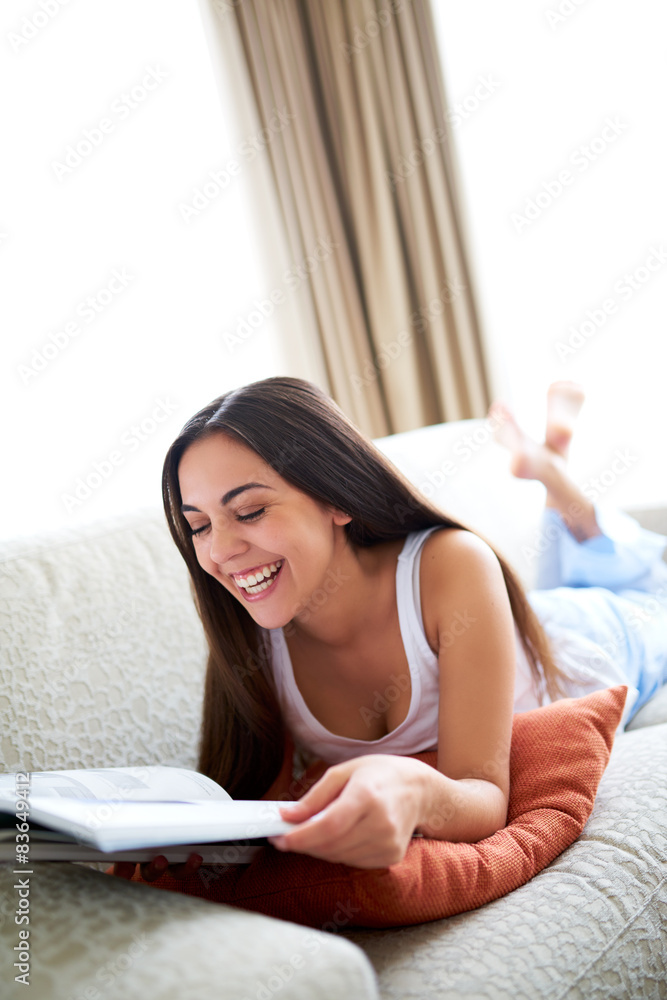 Woman lying on couch reading and laughing. Woman lying on couch reading and laughing.