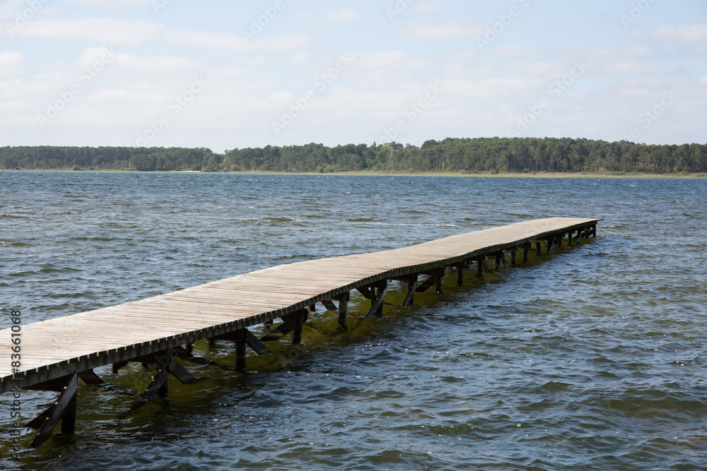 Old wooden pontoon leading to the horizon upon water by blue day