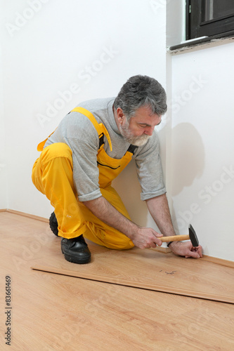 Laminate flooring of room, worker pound in a nail to batten