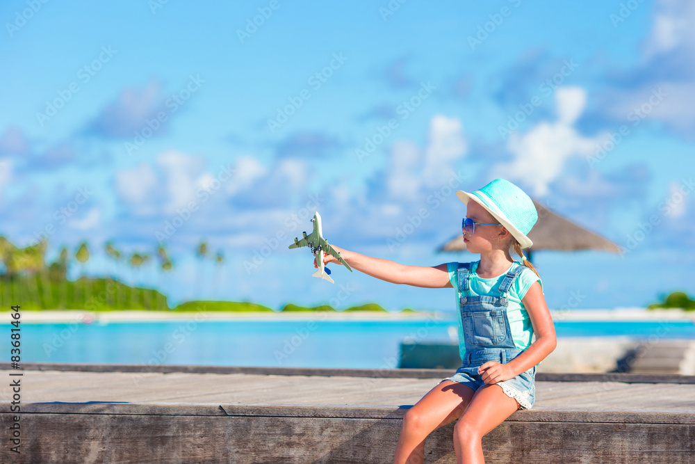 Fototapeta premium Happy little girl with toy airplane in hands on white sandy