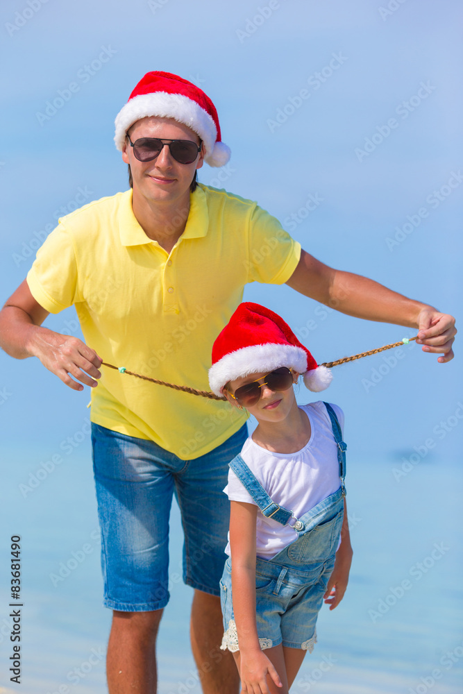 Obraz premium Little girl and happy dad in Santa Hat during beach vacation
