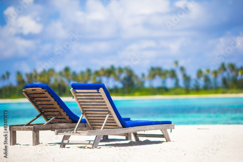 Lounge chairs with bag and hat on tropical white beach 