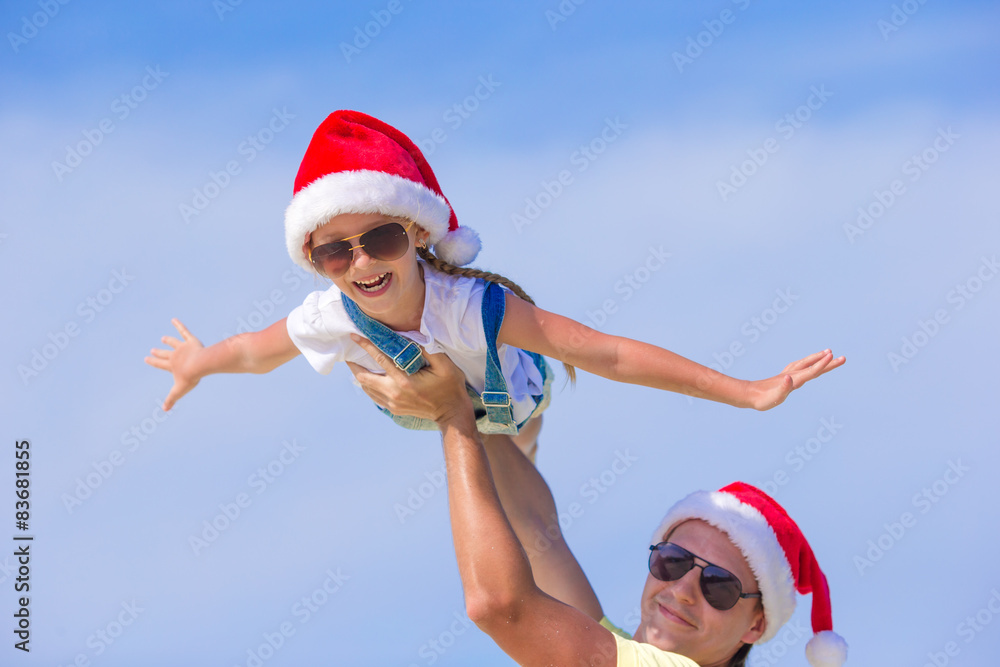 Obraz premium Little girl and happy dad in Santa Hat during beach vacation