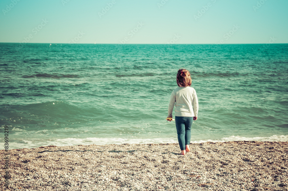 Bambina cammina a piedi nudi sulla spiaggia verso il mare Bambina cammina a piedi nudi sulla spiaggia verso il mare