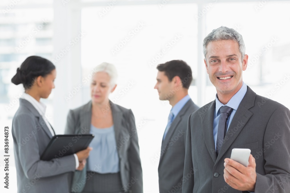 Businessman using a smartphone with colleagues behind in office Businessman using a smartphone with colleagues behind in office