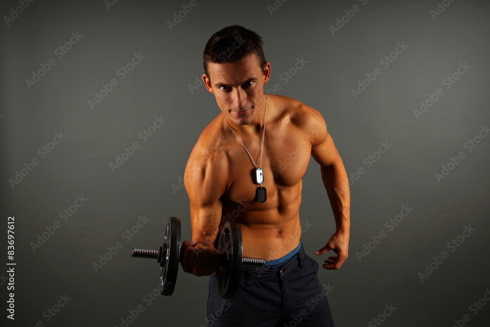 Young man exercises with dumbbell on the gray background