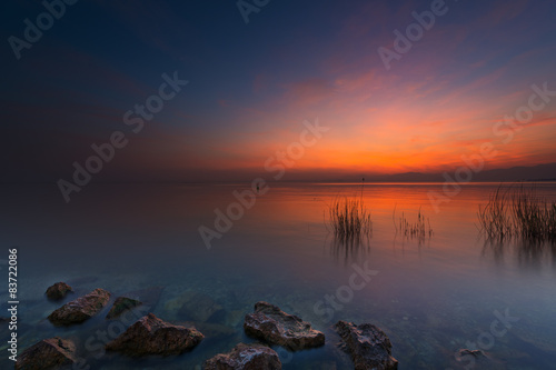 Fototapeta Naklejka Na Ścianę i Meble -  rocks and grass in lake at red orange sunset in italy