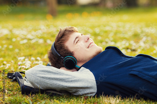 Student relaxing lying on grass and listening to music.