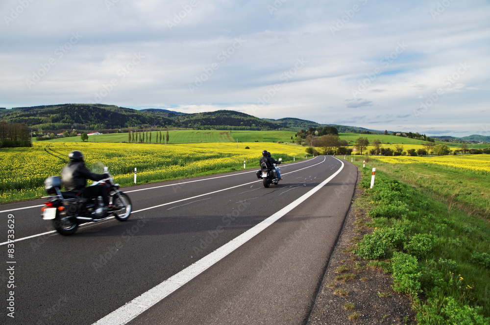 Motorcycles traveling on road between blooming rape fields Motorcycles traveling on road between blooming rape fields