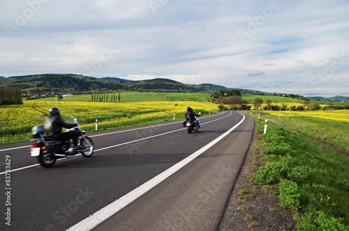 Motorcycles traveling on road between blooming rape fields
