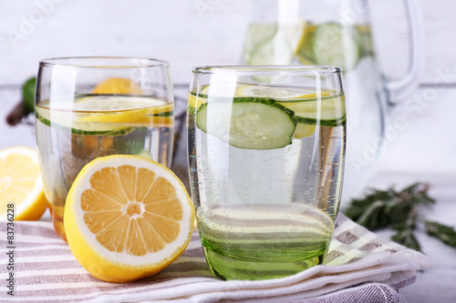 Fresh water with lemon and cucumber in glassware on wooden table, closeup