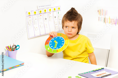 Boy holding carton clock sitting at the table