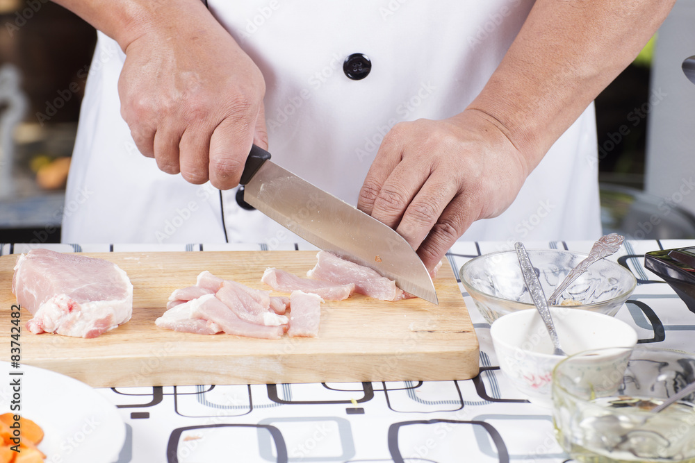Close up of Hand's Chef cutting raw pork on wooden board