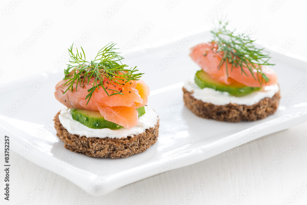 canape with cheese, cucumber and salted salmon on white plate