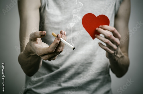 smoker holds the cigarette in his hand and a red heart in studio