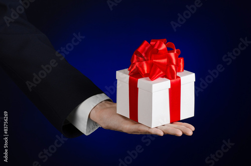 man in a black suit holding gift wrapped in white box in studio