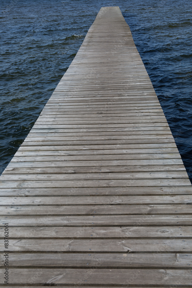 Old wooden pontoon leading to the horizon upon water by blue day Old wooden pontoon leading to the horizon upon water by blue day