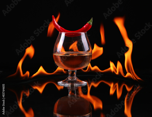 Hot chili pepper in a cognac ballon with a fire on a black 