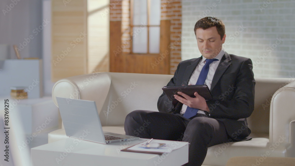 Businessman typing, scrolling pages on tablet, looking at camera Businessman typing, scrolling pages on tablet, looking at camera