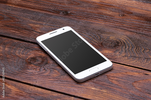 Smart phone with blank screen lying on wooden table