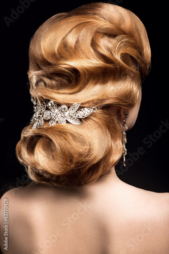 Beautiful red-haired girl in a black dress with a smooth evening haircut in the form of waves and bright makeup. Beauty face. Picture taken in the studio on a black background.