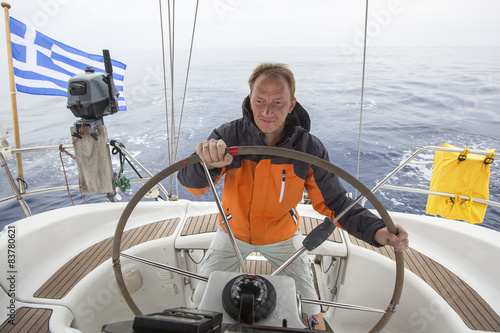 Young skipper drives the sailboat in the open sea. 