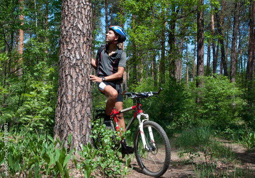 Cyclist leaning on pine tree in a beautiful spring forest. 