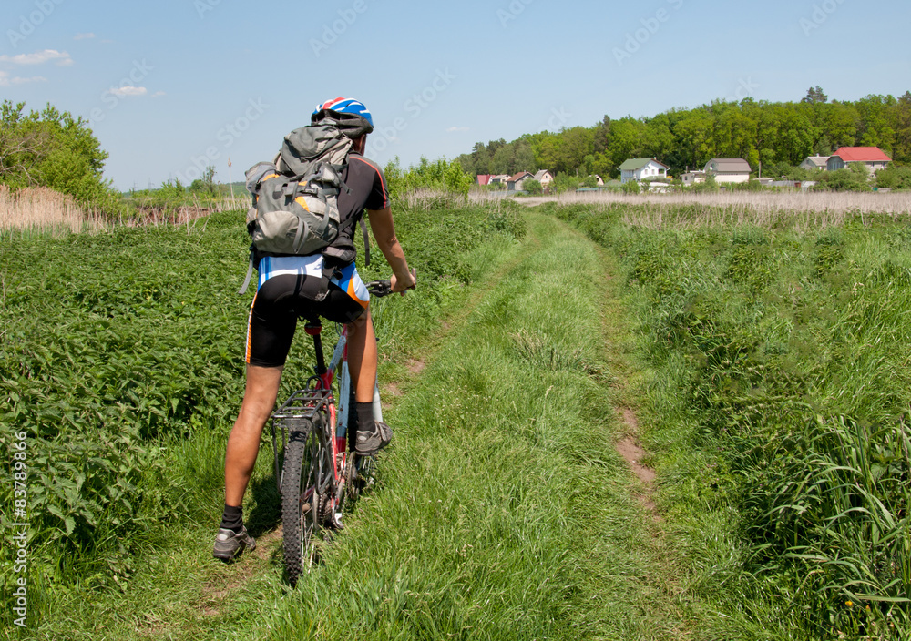 Cyclist riding a mountain bike in direction of the village Cyclist riding a mountain bike in direction of the village