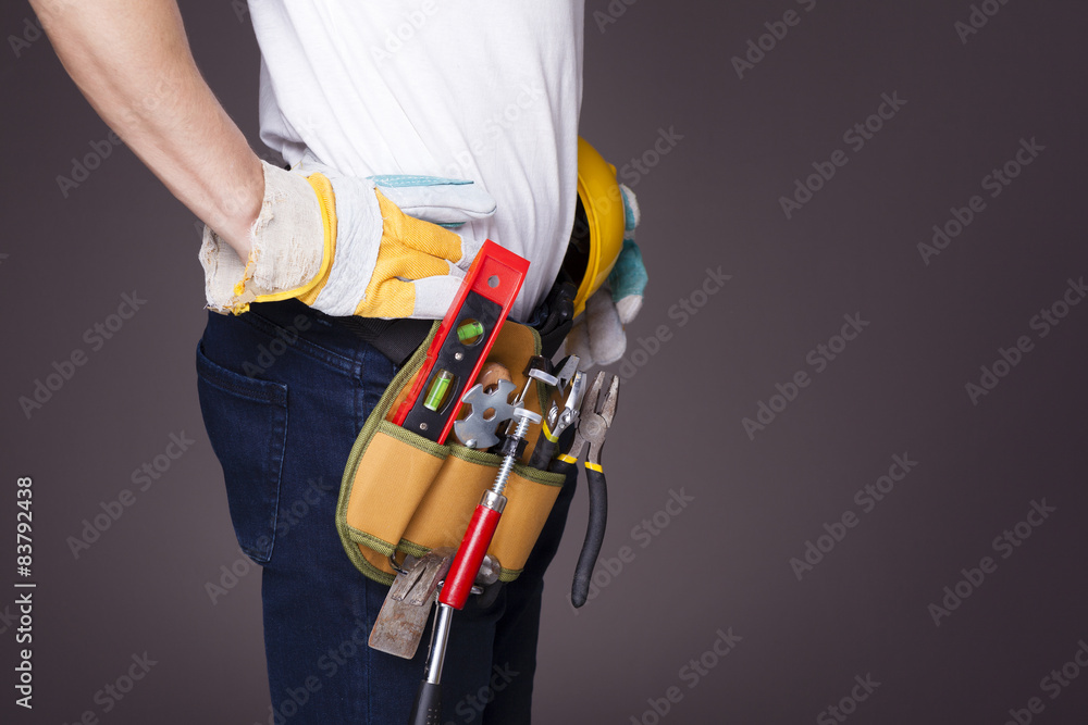 Side view of a worker with toolbelt and helmet against dark back Side view of a worker with toolbelt and helmet against dark back