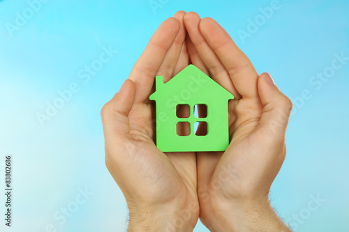 Female hands holding house on turquoise background