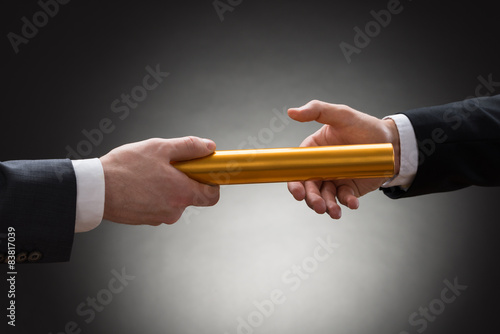 Two Hands Passing A Golden Relay Baton