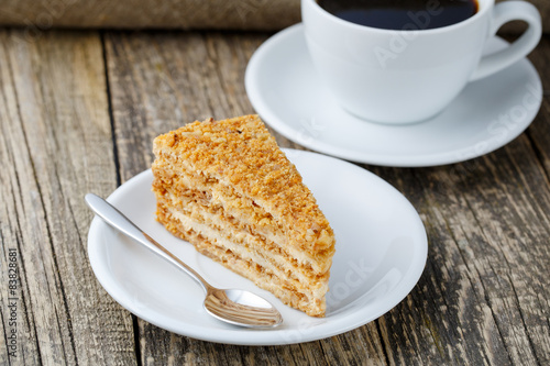 Tasty honey cake with cup of coffee on wooden background.