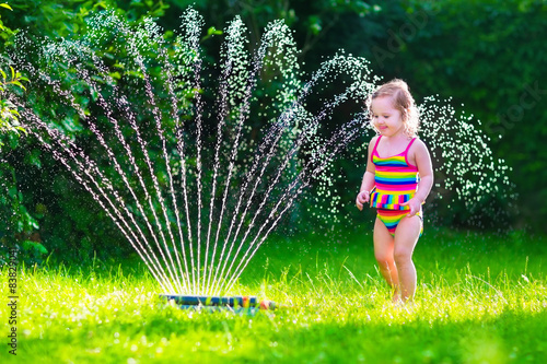Little girl playing with garden water sprinkler