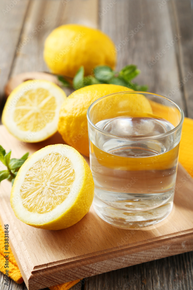 Lemons on cutting board with glass of water on grey wooden backg Lemons on cutting board with glass of water on grey wooden backg