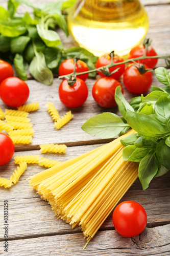 Spaghetti, basil and tomatoes on grey wooden background